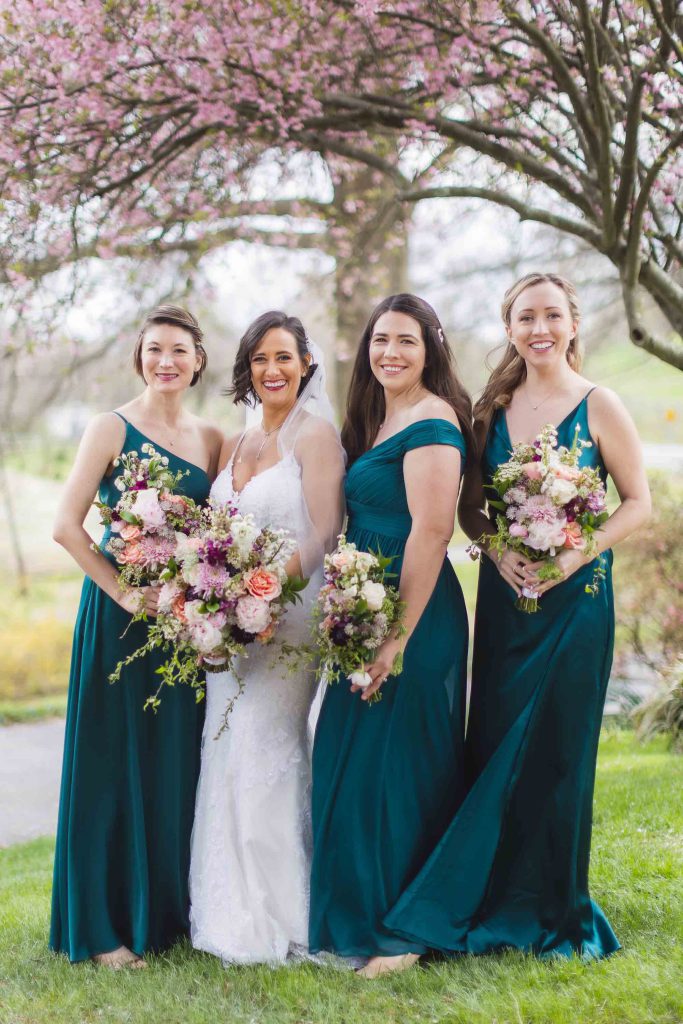 Four bridesmaids in teal dresses pose for a wedding portrait.