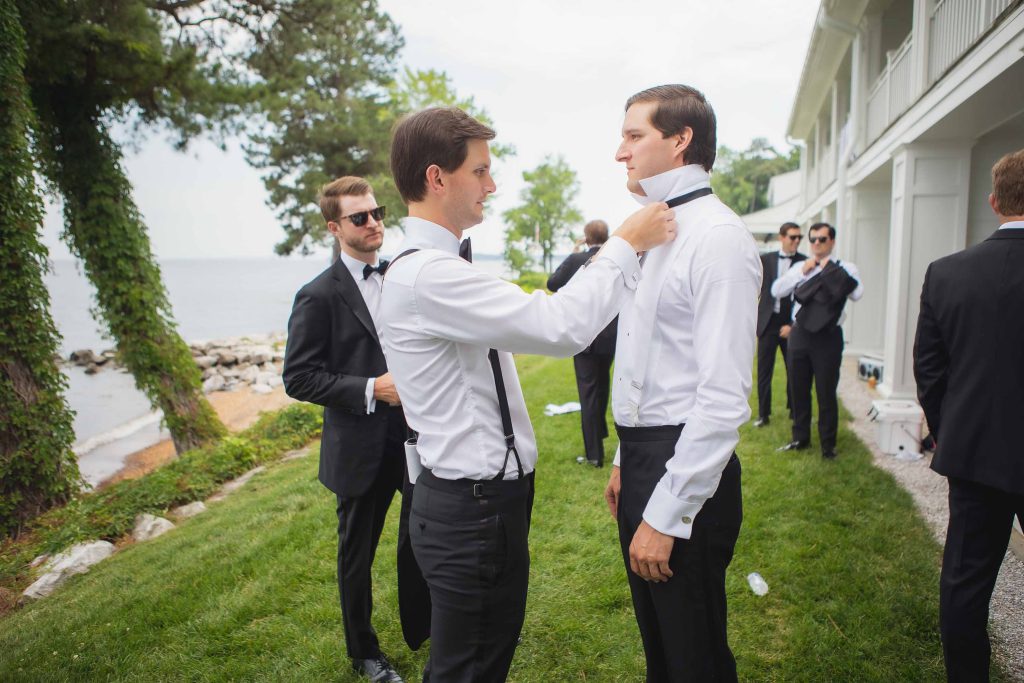 Candid groomsmen adjusting their ties during wedding preparation.