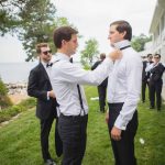 Candid groomsmen adjusting their ties during wedding preparation.
