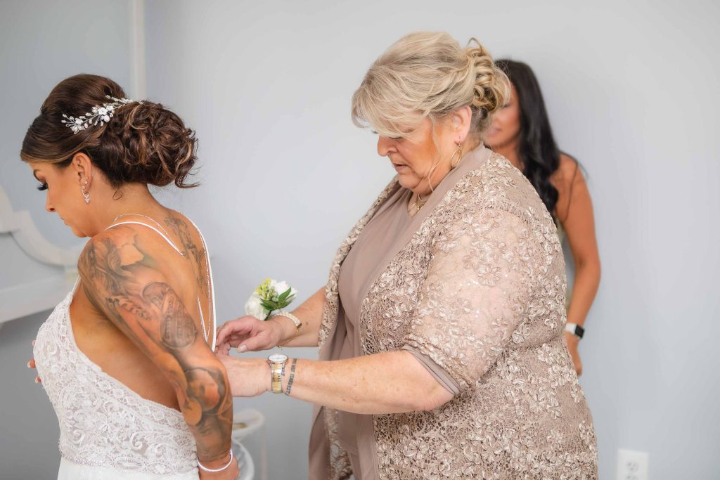 A woman is assisting her mother in putting on her wedding dress during the candid preparation.