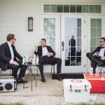 Three men in tuxedos candidly preparing for a wedding on the porch of a house.