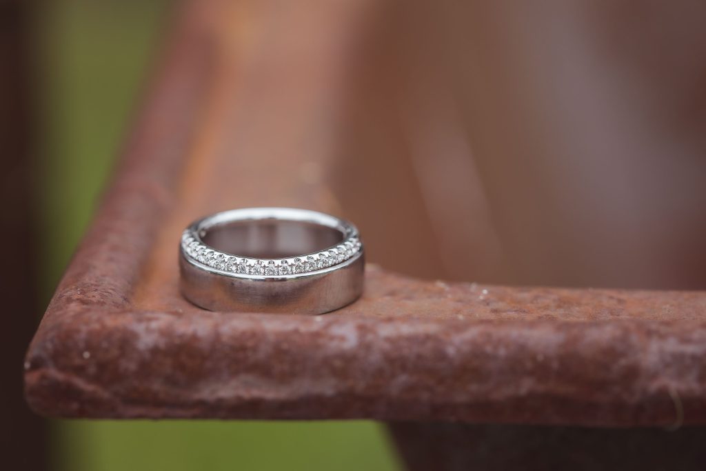 A silver wedding ring sits on top of a metal bowl, showcasing intricate details.
