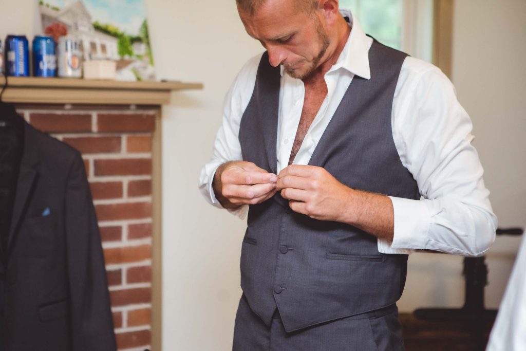 A man is preparing for a wedding, adjusting his vest in front of a mirror.