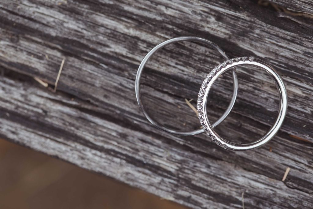 Two silver wedding rings laying on top of a wooden surface.