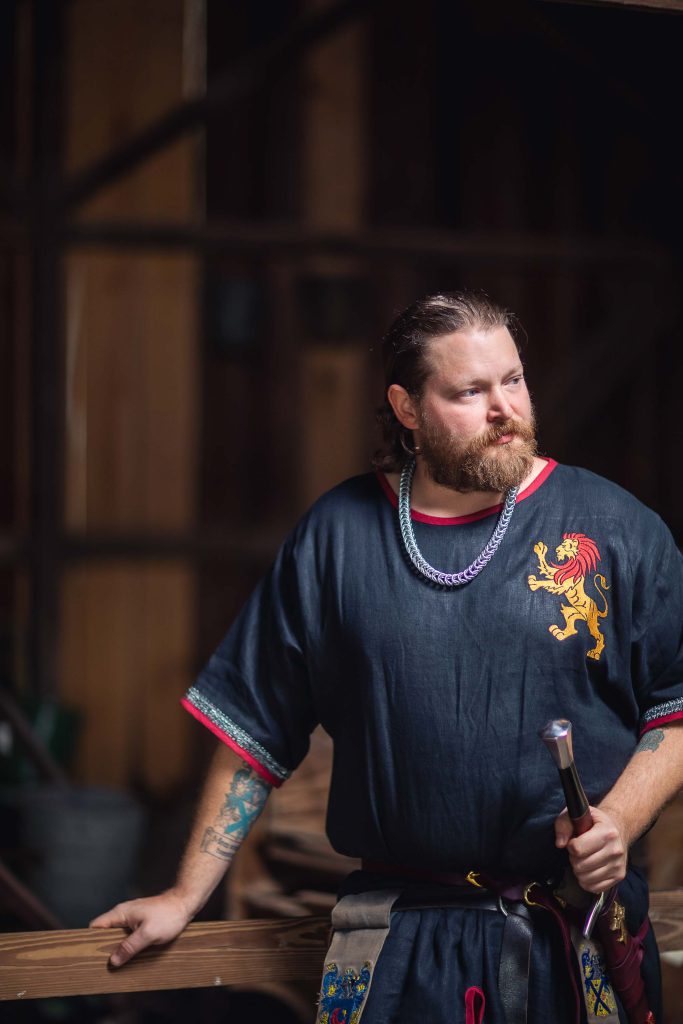 A man in a medieval costume holding a sword for a portrait shoot at a wedding.