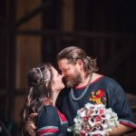 A medieval groom and bride share a passionate kiss during their wedding portrait session in front of a wooden barn.