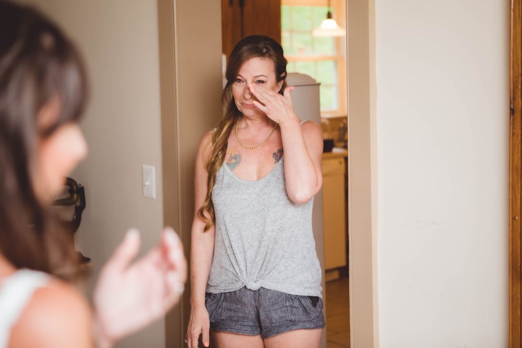 A candid woman prepares for her wedding as she sheds tears in front of a mirror.