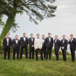 A group of groomsmen in tuxedos standing in front of the ocean for a wedding portrait.