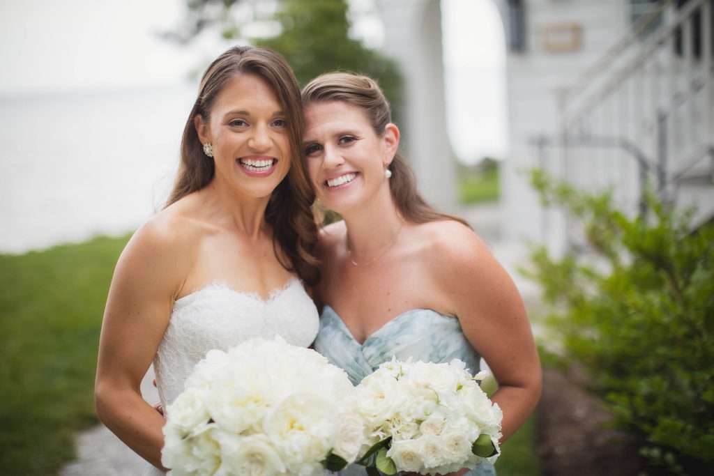 Portrait of two bridesmaids holding bouquets in front of a house on a wedding day.
