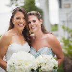 Portrait of two bridesmaids holding bouquets in front of a house on a wedding day.