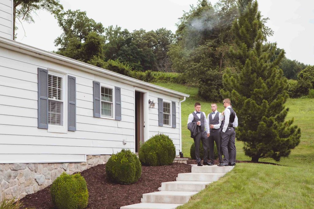 Three groomsmen standing on steps during wedding preparations.