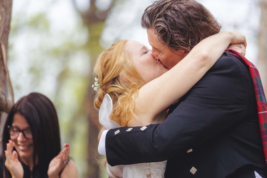 A wedding ceremony in the woods with a bride and groom kissing.