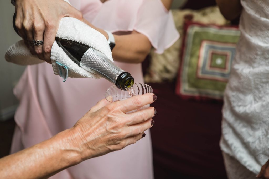 A candid bride pours wine for her bridesmaids during wedding preparation.