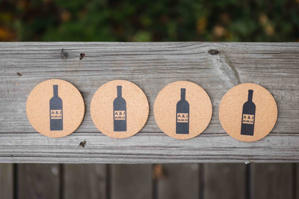Four wedding wine bottle coasters on a wooden fence.