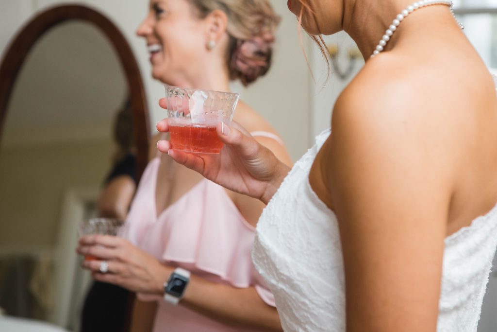 Two candid bridesmaids preparing for a wedding in front of a mirror.