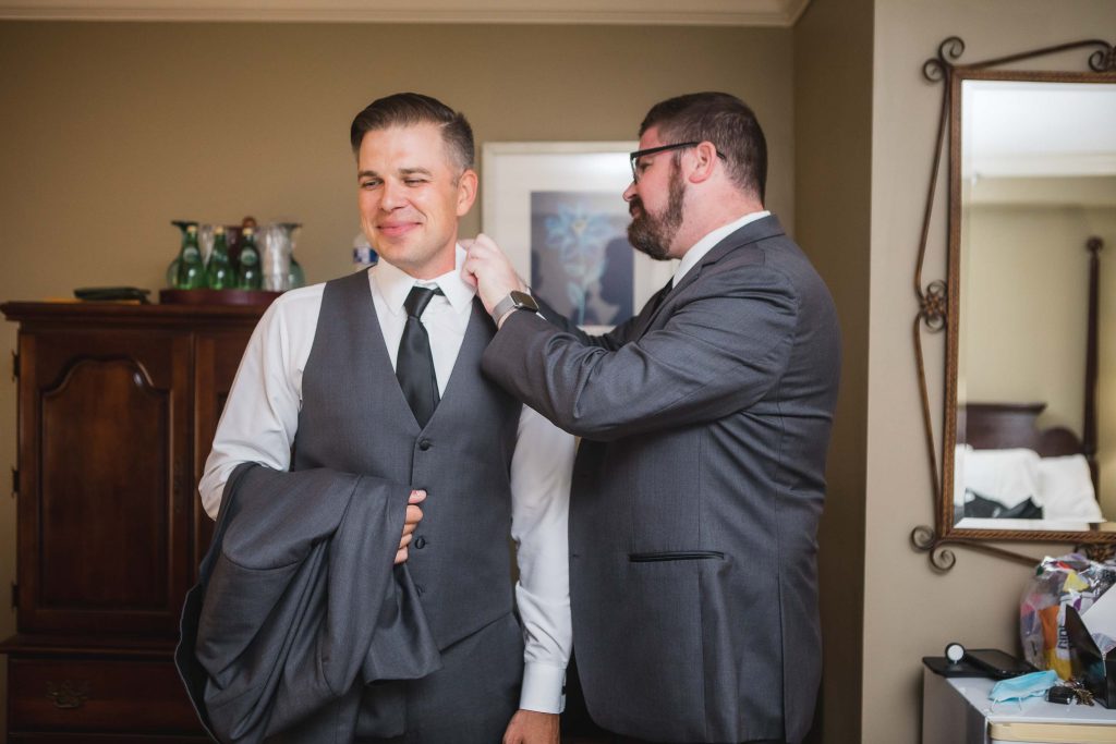 A candid moment of preparation as a man puts on a tie for a man in a suit at a wedding.