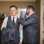 A candid moment of preparation as a man puts on a tie for a man in a suit at a wedding.