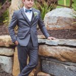 A groom in a gray suit posing for a wedding portrait against a stone wall.