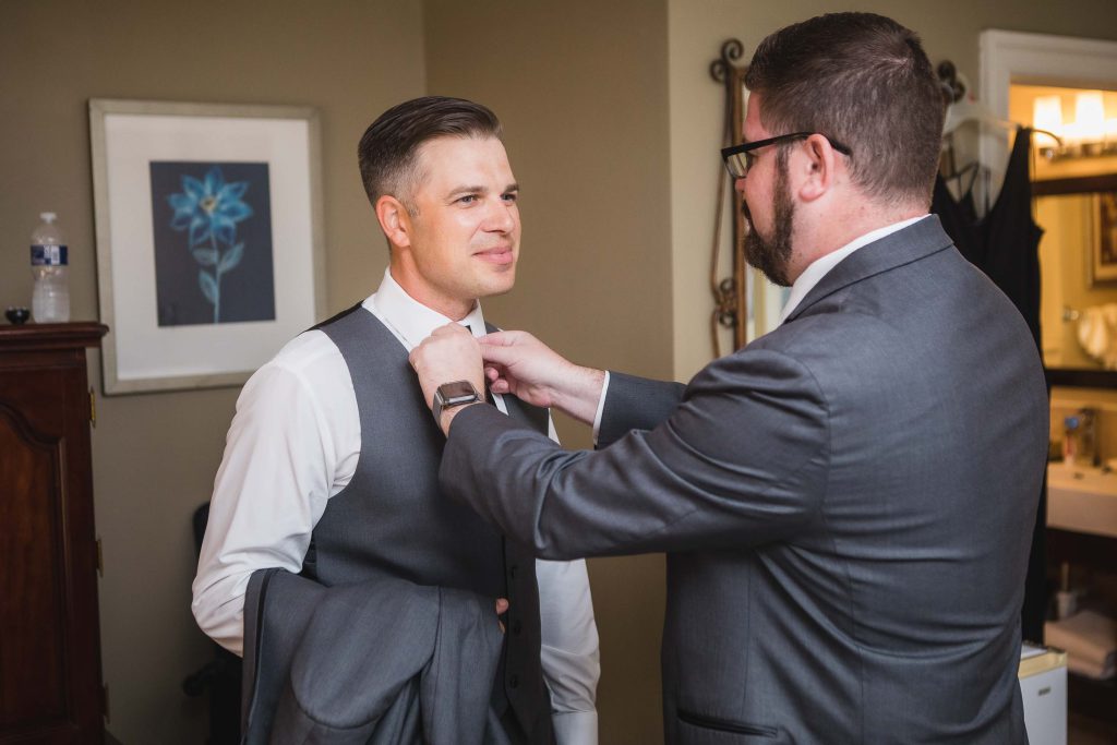 A groom preparing for his wedding by candidly putting on a tie.