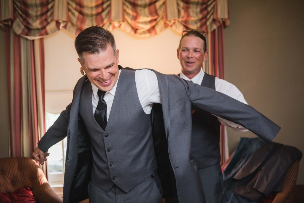 Two groomsmen preparing for a wedding, candidly putting on their jackets in a room.