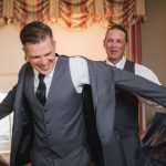 Two groomsmen preparing for a wedding, candidly putting on their jackets in a room.
