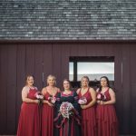 Red bridesmaids standing in front of a barn for a wedding portrait.