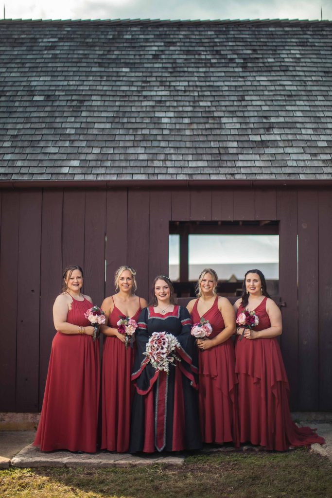Red bridesmaids standing in front of a barn for a wedding portrait.
