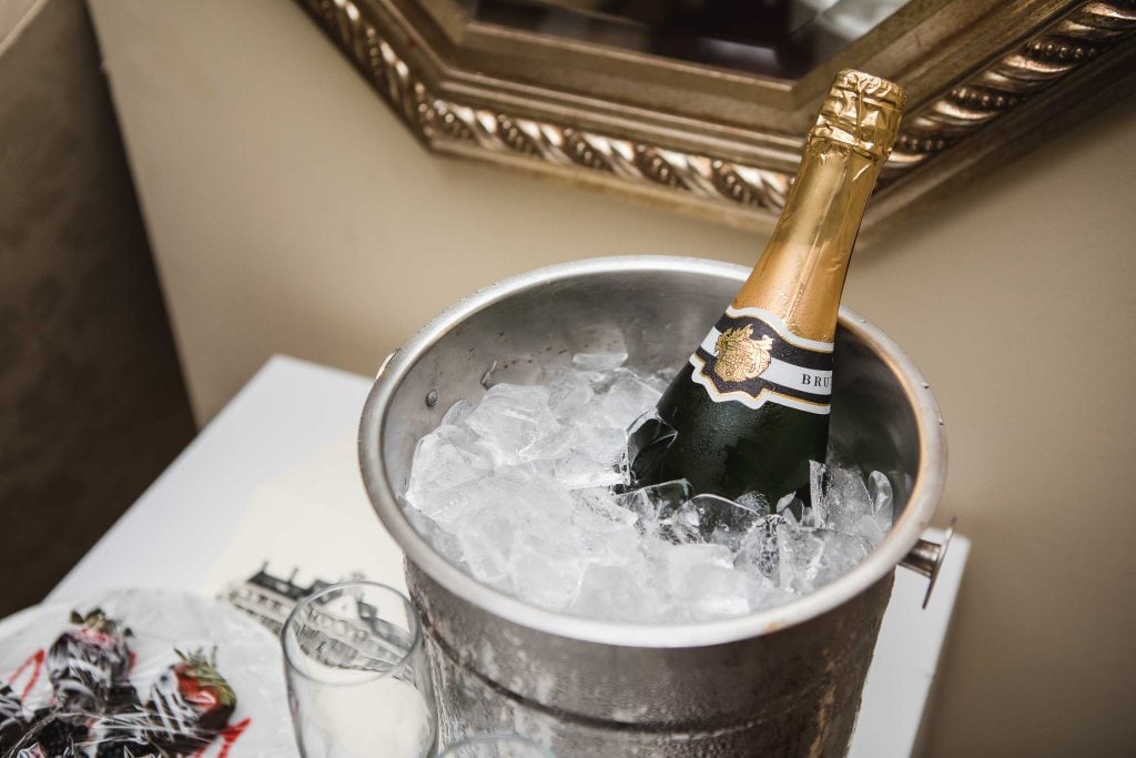 A bottle of champagne in an ice bucket with wedding details reflected in a mirror.