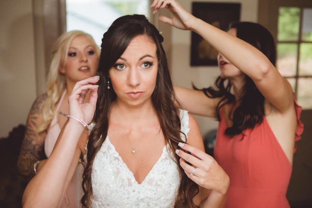 A bride is getting candidly prepared for her wedding by her bridesmaids.