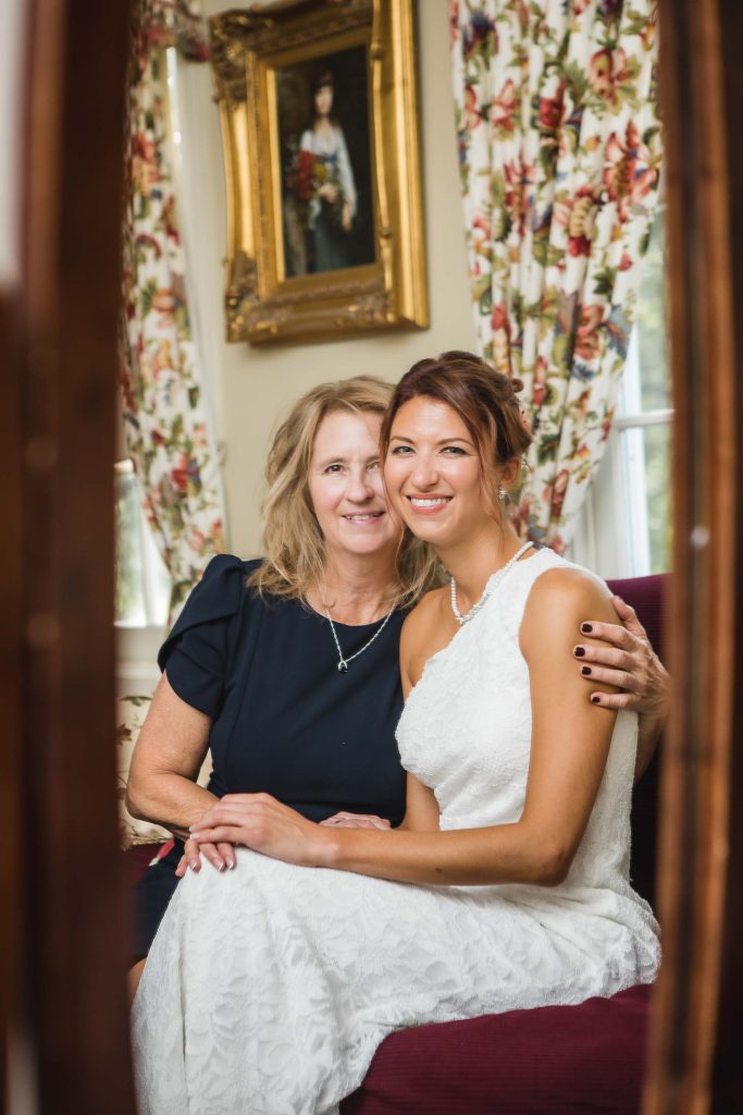 A candid bride and her mother preparing for a wedding in front of a mirror.