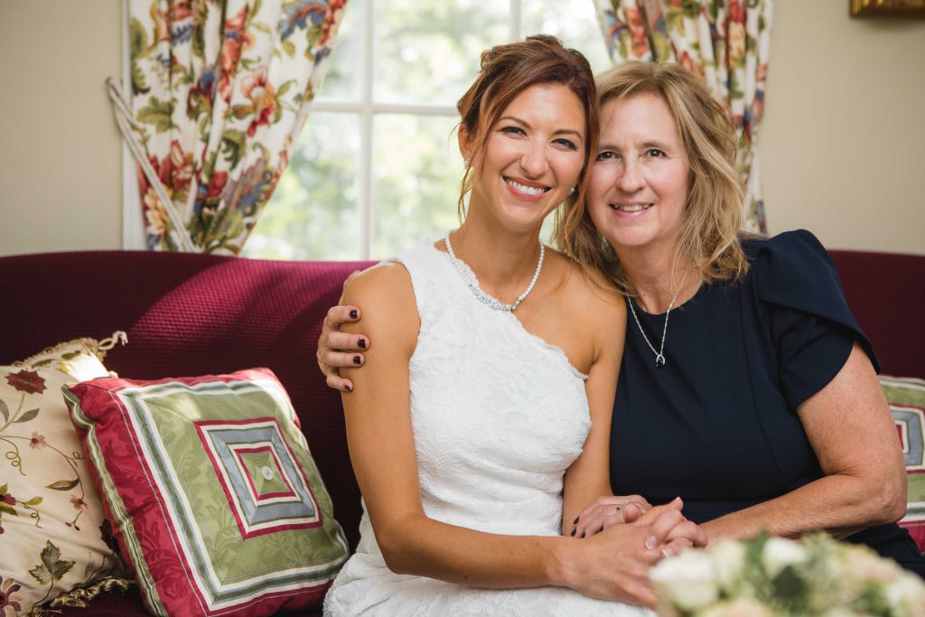A bride and her mother candidly preparing for the wedding on a couch.