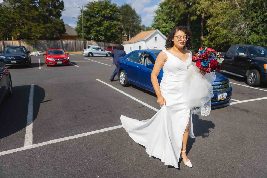 A candid bride in a white dress preparing for her wedding in a parking lot.