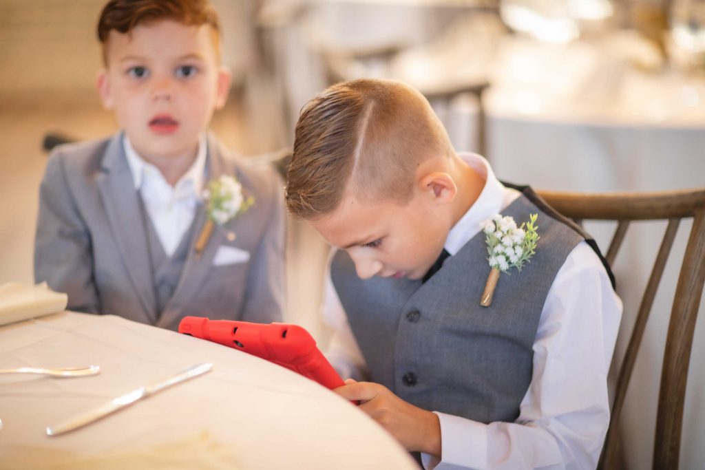 Candid preparation at a wedding with two young boys using a tablet computer.