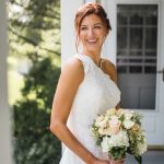 A wedding portrait of a bride in a white dress holding her bouquet on a porch.