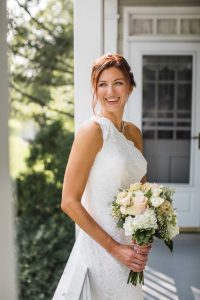 A wedding portrait of a bride in a white dress holding her bouquet on a porch.