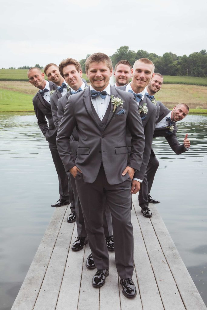 A group of groomsmen posing for a wedding portrait on a dock.