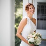 A wedding bride smiles while holding her bouquet on the porch.