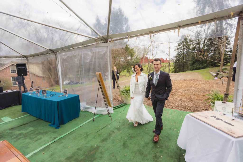 A wedding couple strolling through a tent at their reception.