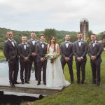 A portrait of groomsmen and bridesmaids on a dock at a wedding.