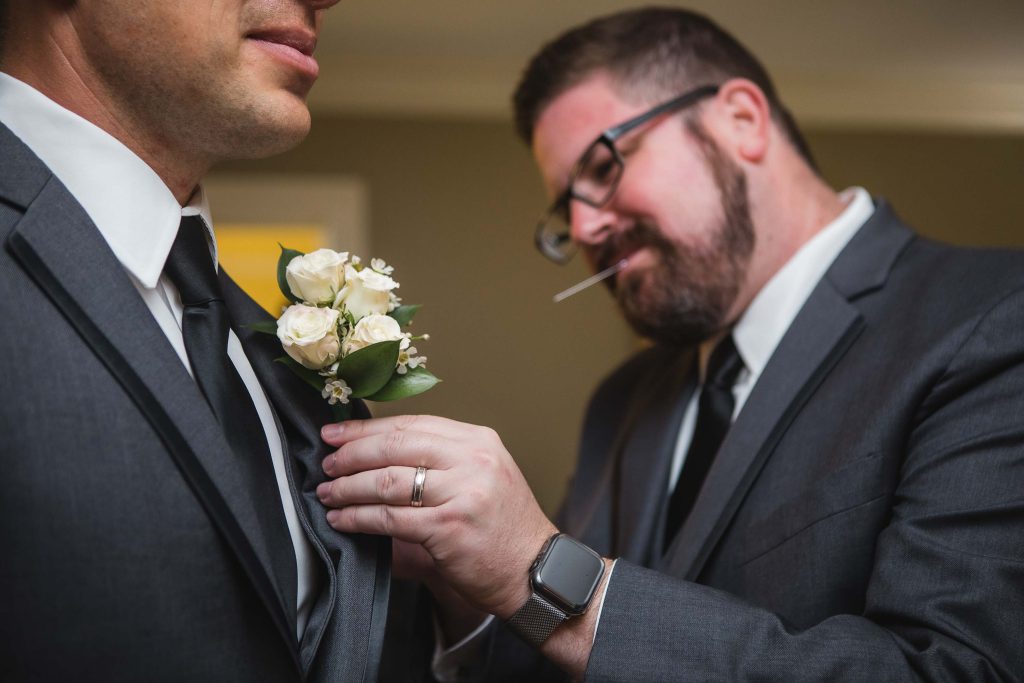 A groom is adjusting his boutonniere before the wedding ceremony.