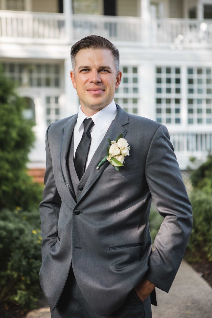 A groom in a wedding suit standing in front of a house.