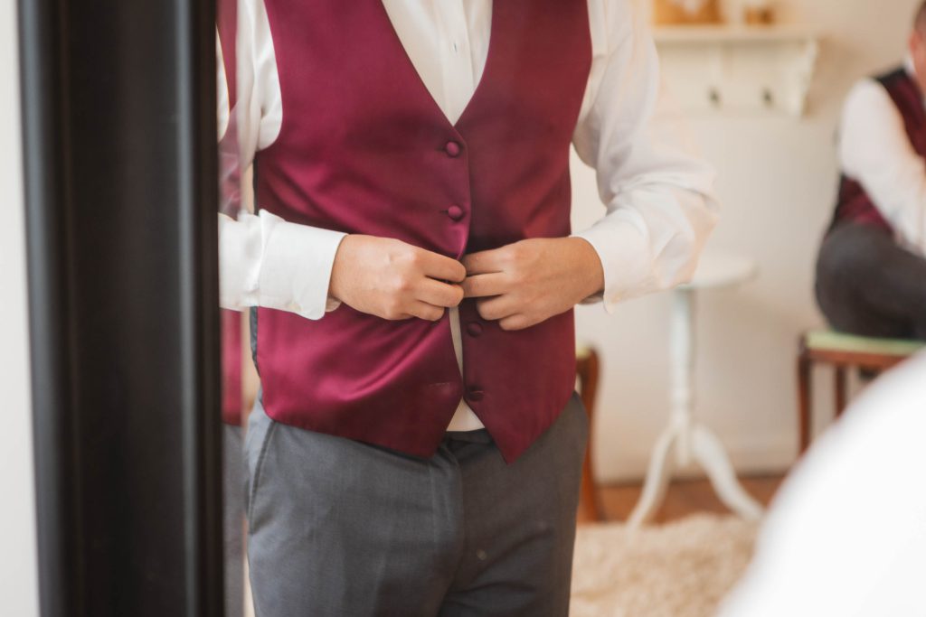 A man is candidly adjusting his vest in front of a mirror.