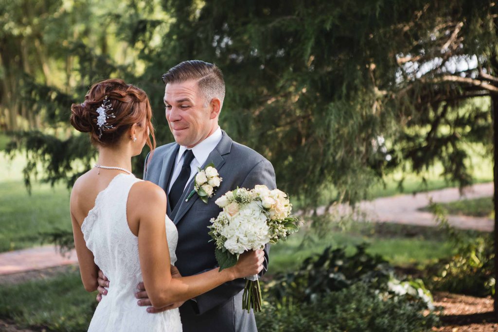 A candid wedding moment as the bride and groom look at each other in front of a tree.