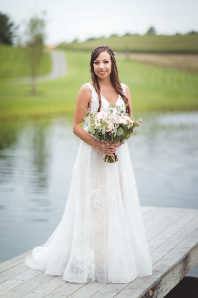 A wedding portrait of a bride holding her bouquet on a dock.