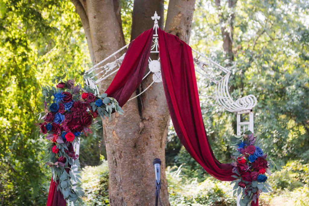 A meticulously decorated wedding arch adorned with red and blue flowers exudes enchanting details.