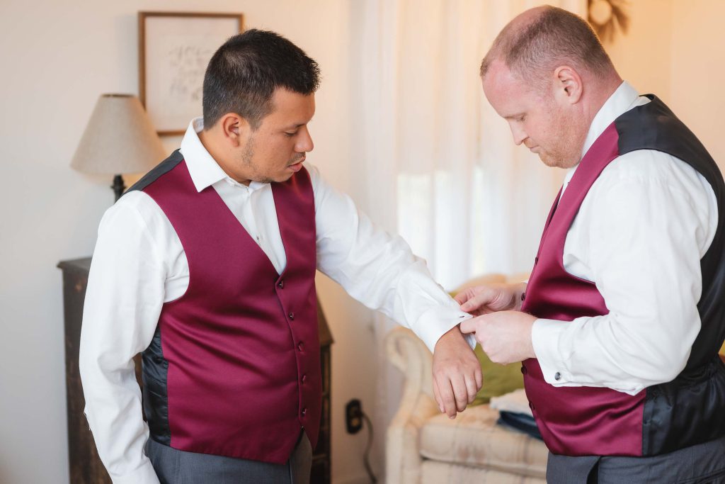 Two men candidly adjusting their vests during wedding preparation.