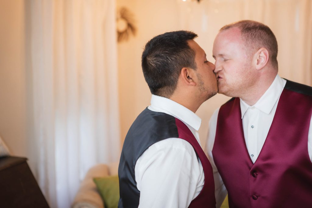 Two grooms candidly preparing for their wedding in front of a mirror.