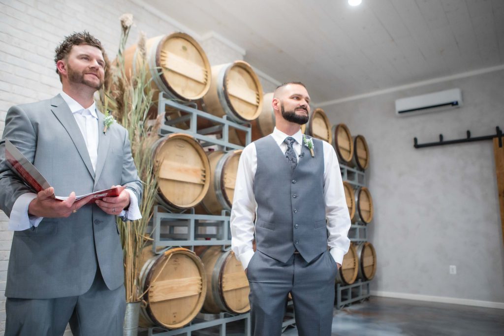 Two grooms preparing for their wedding ceremony in front of wine barrels.