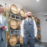 Two grooms preparing for their wedding ceremony in front of wine barrels.