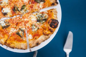 A slice of pizza on a plate next to a fork with wedding details.